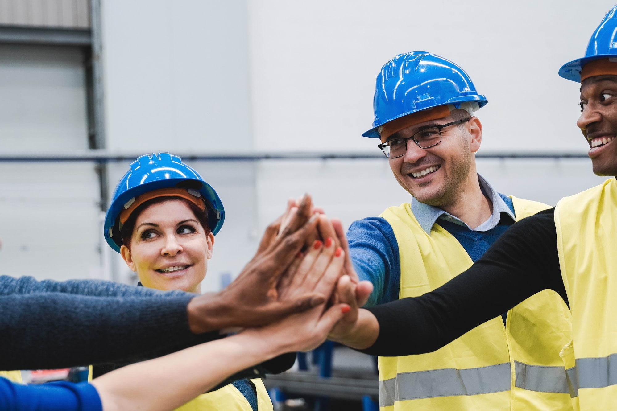 Happy multiracial engineer stacking hands while working at robotics warehouse