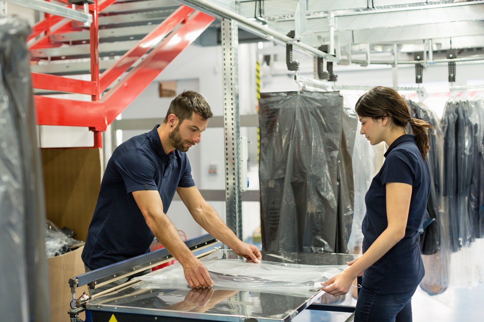 Warehouse workers wrapping garment stock in plastic in distribution warehouse