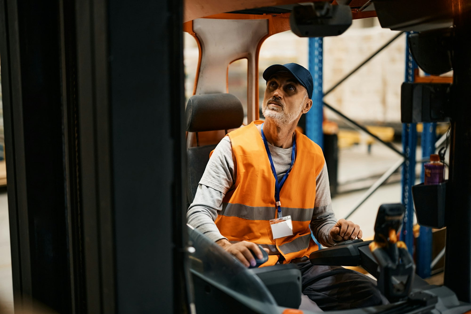 Mature warehouse worker moving pallets with forklift in industrial building.